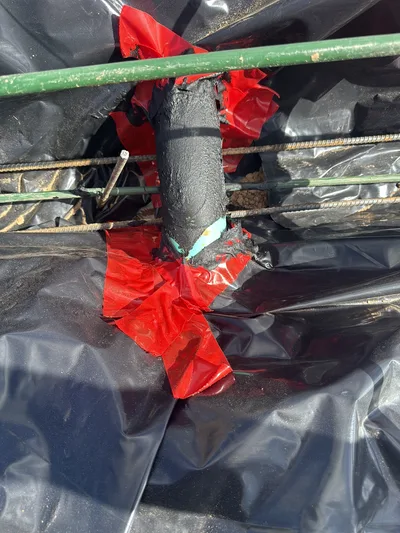 Plumbing pipe penetration sealed with tape through a vapor barrier before a concrete pour.