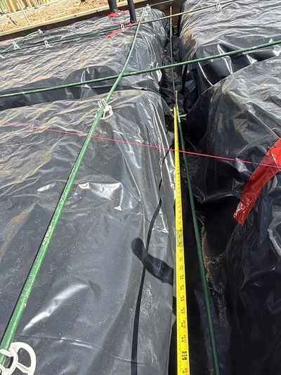 Tape measure checking post-tension cable spacing over a vapor barrier before concrete placement.